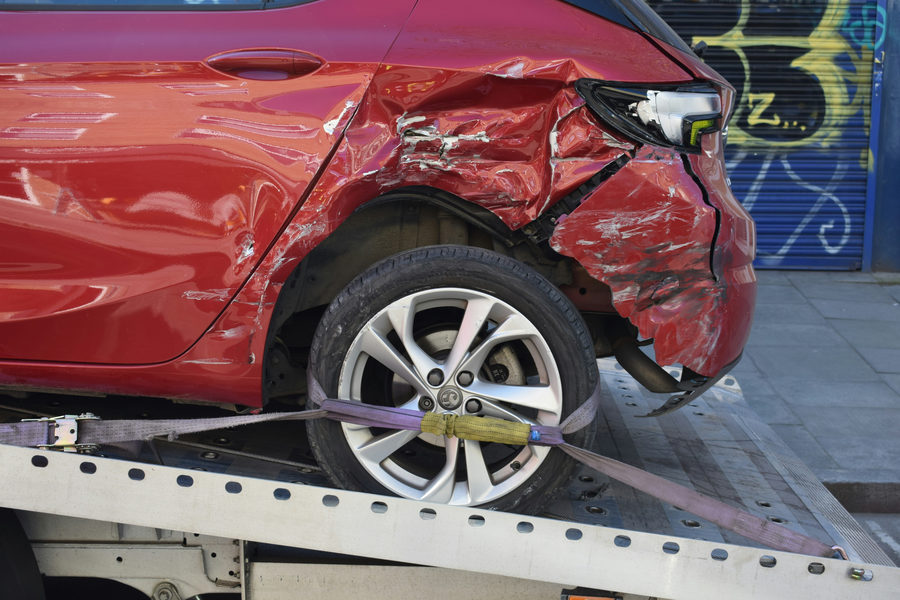 Red car with crash damage on the front bumper being on emergency towing