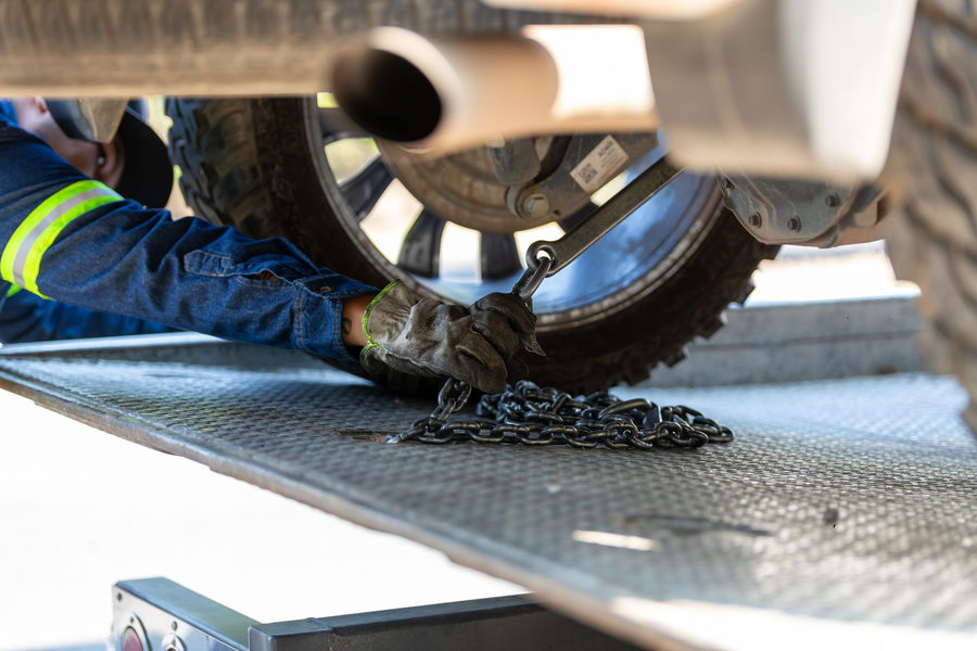 Man fastening the wheel of car onto a towtruck using steel chains.